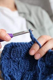 Photo of Woman crocheting with hook and blue yarn, closeup