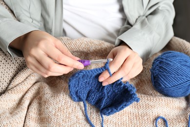 Photo of Woman crocheting with hook and blue yarn, closeup