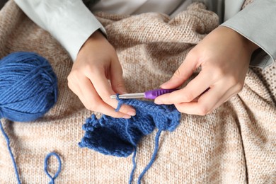 Photo of Woman crocheting with hook and blue yarn, top view