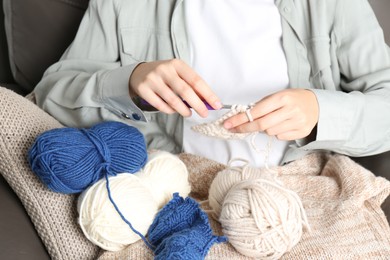 Photo of Woman crocheting with hook and beige yarn, closeup