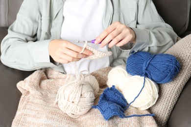 Photo of Woman crocheting with hook and beige yarn, closeup