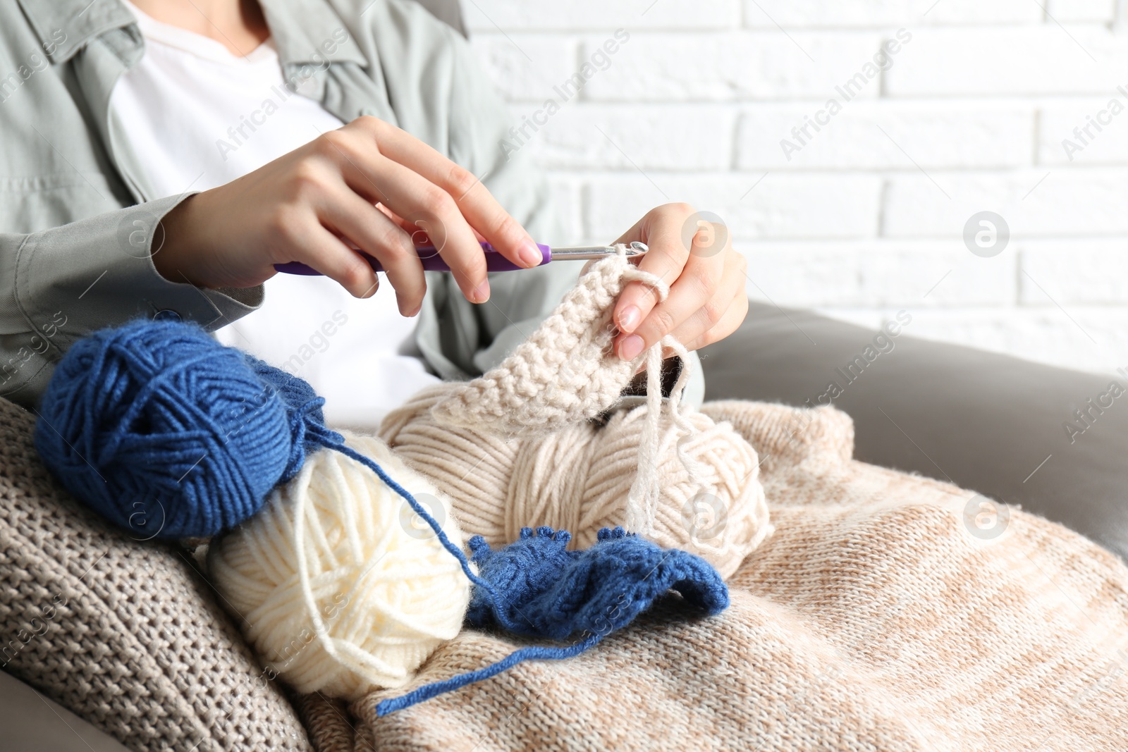 Photo of Woman crocheting with hook and beige yarn at home, closeup