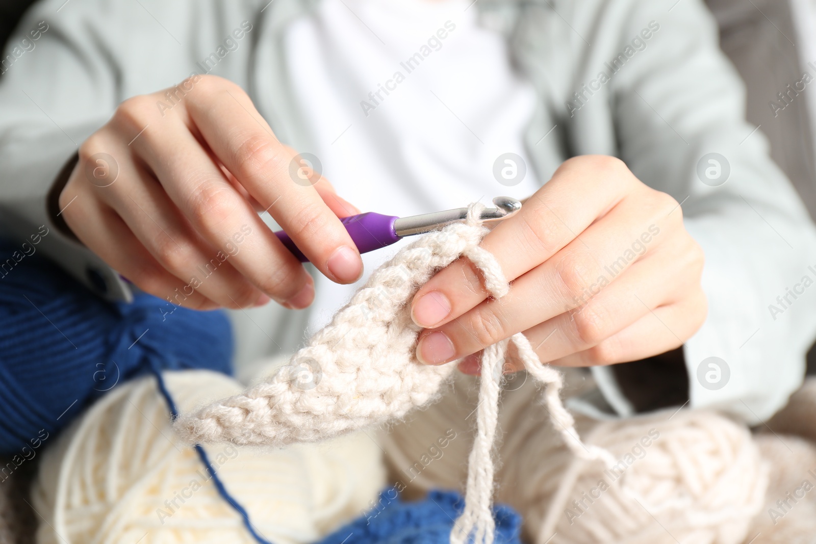 Photo of Woman crocheting with hook and beige yarn, closeup