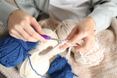 Photo of Woman crocheting with hook and beige yarn, above view