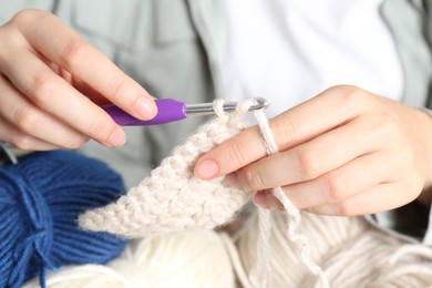 Photo of Woman crocheting with hook and beige yarn, closeup