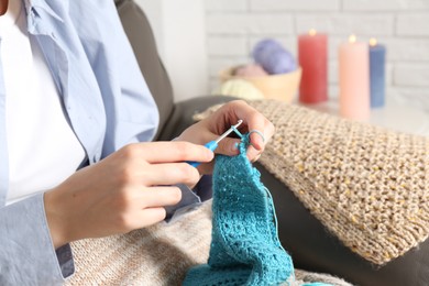 Woman crocheting with hook and yarn at home, closeup