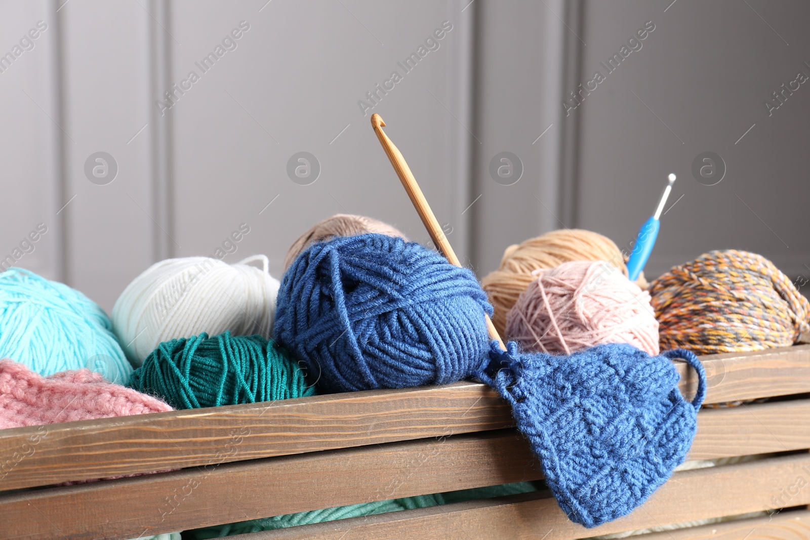 Photo of Different yarns, pattern sample and crochet hooks in wooden crate, closeup