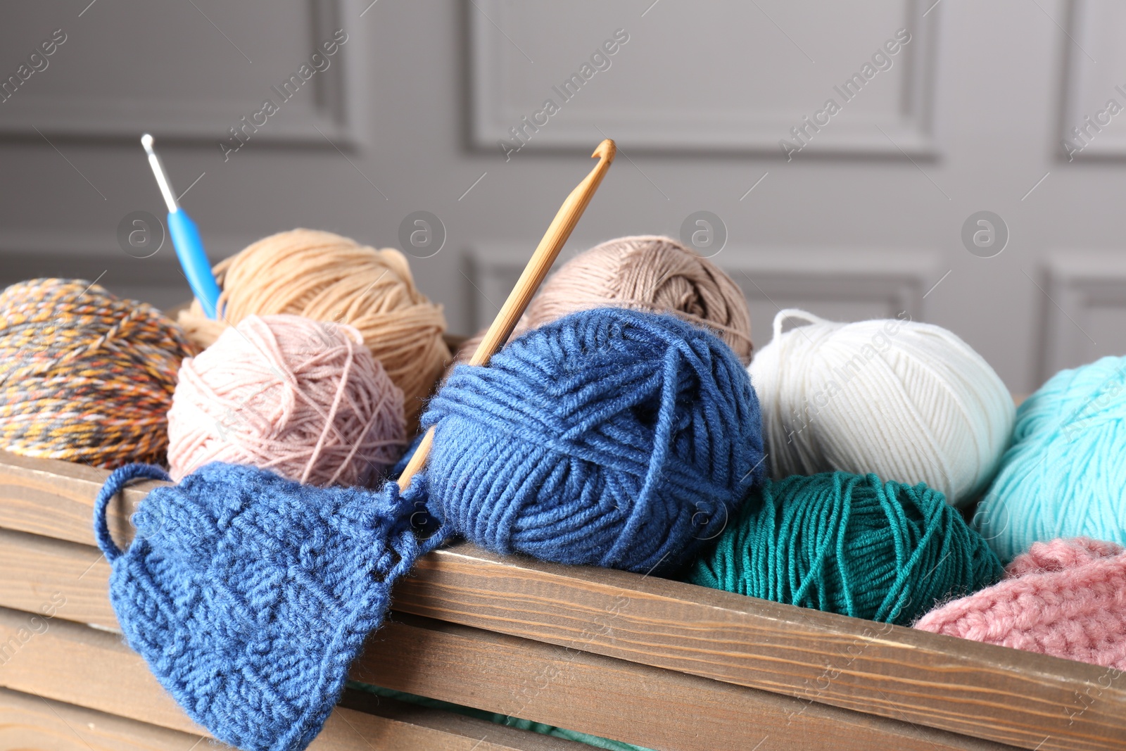 Photo of Different yarns, pattern sample and crochet hooks in wooden crate, closeup