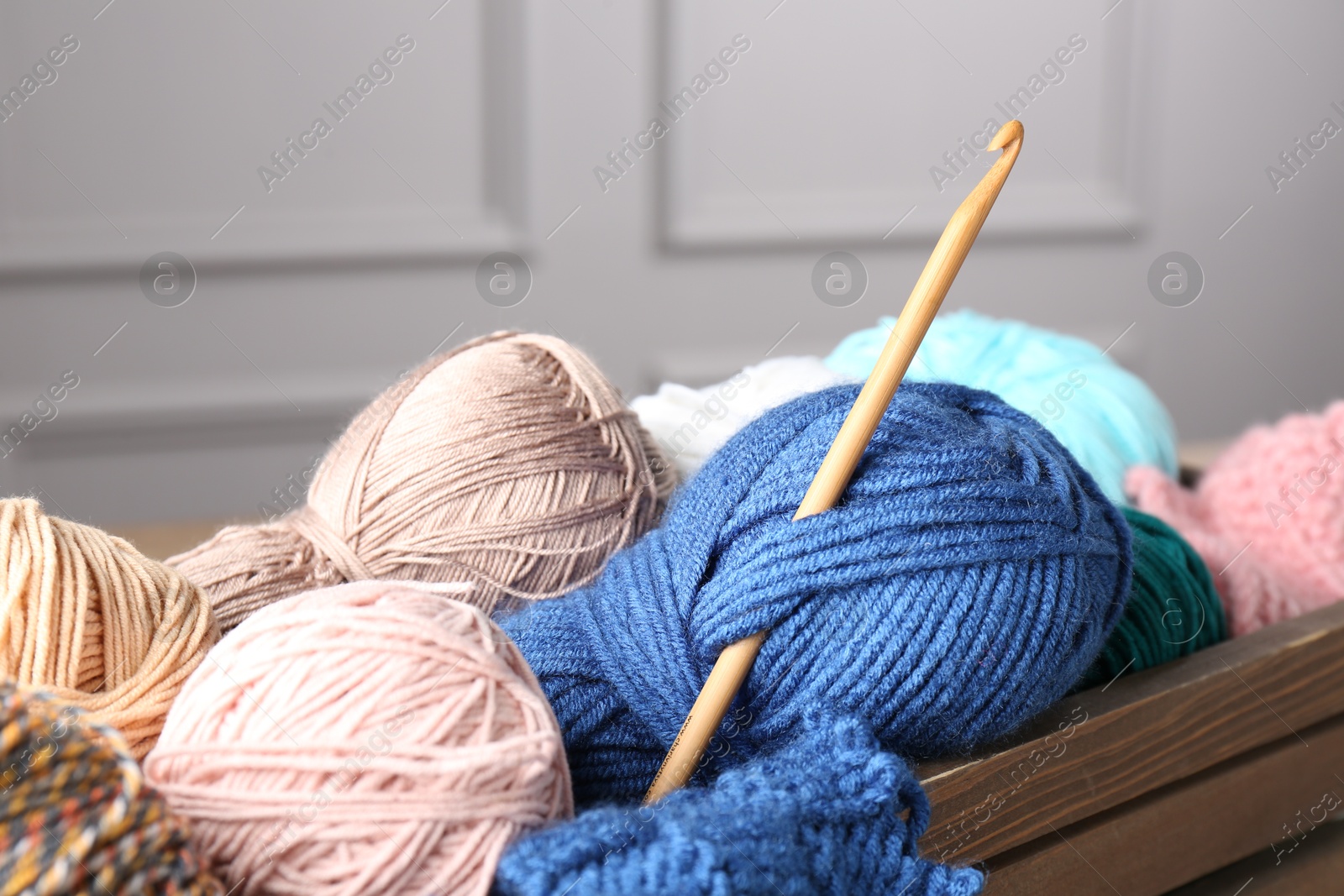 Photo of Different yarns and crochet hook in wooden crate, closeup