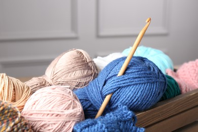 Photo of Different yarns and crochet hook in wooden crate, closeup