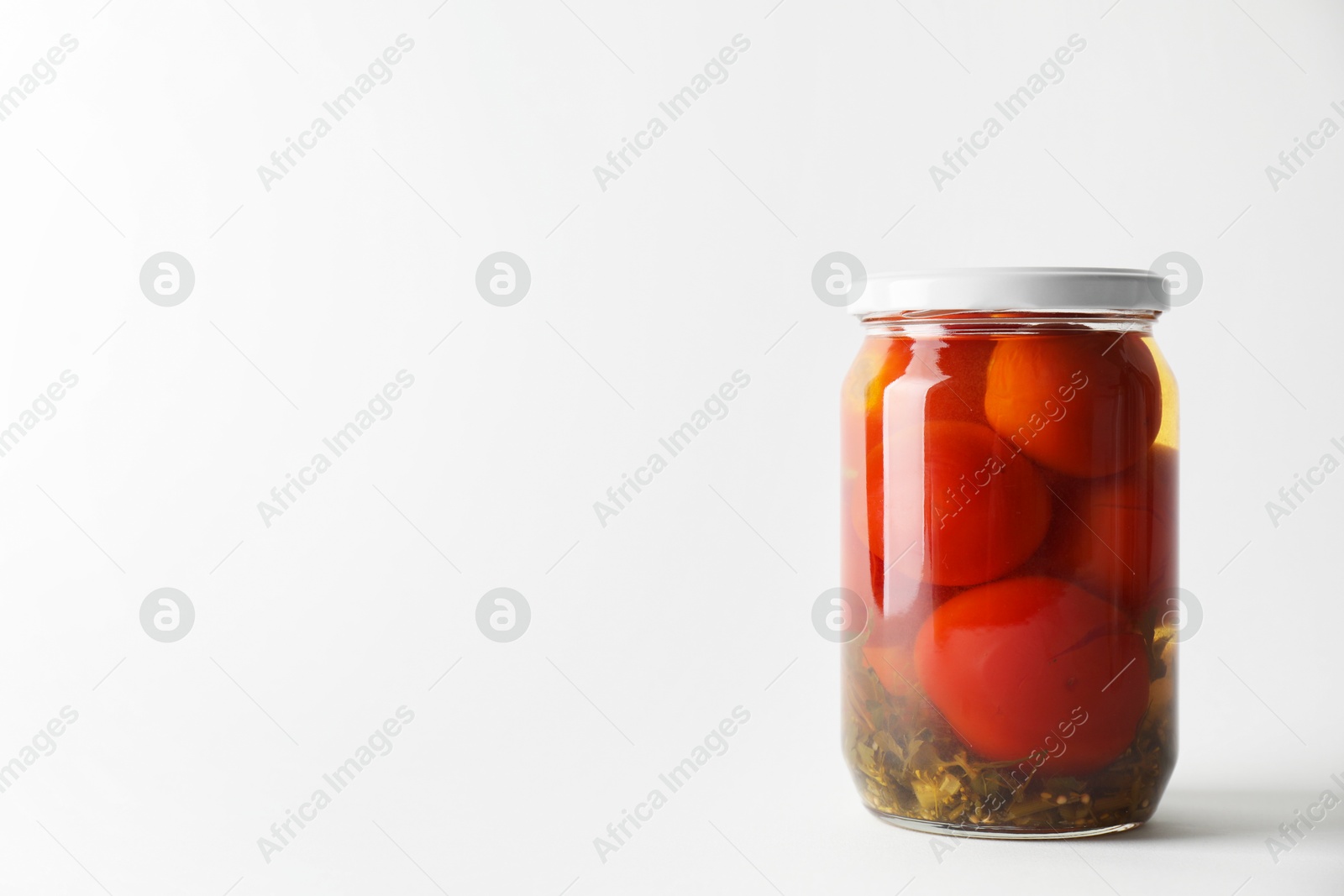 Photo of Tasty pickled tomatoes in jar on light grey background. Space for text