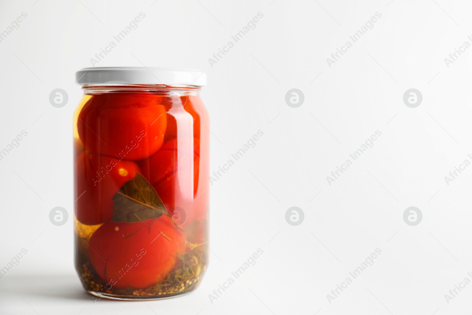 Photo of Tasty pickled tomatoes in jar on light grey background. Space for text