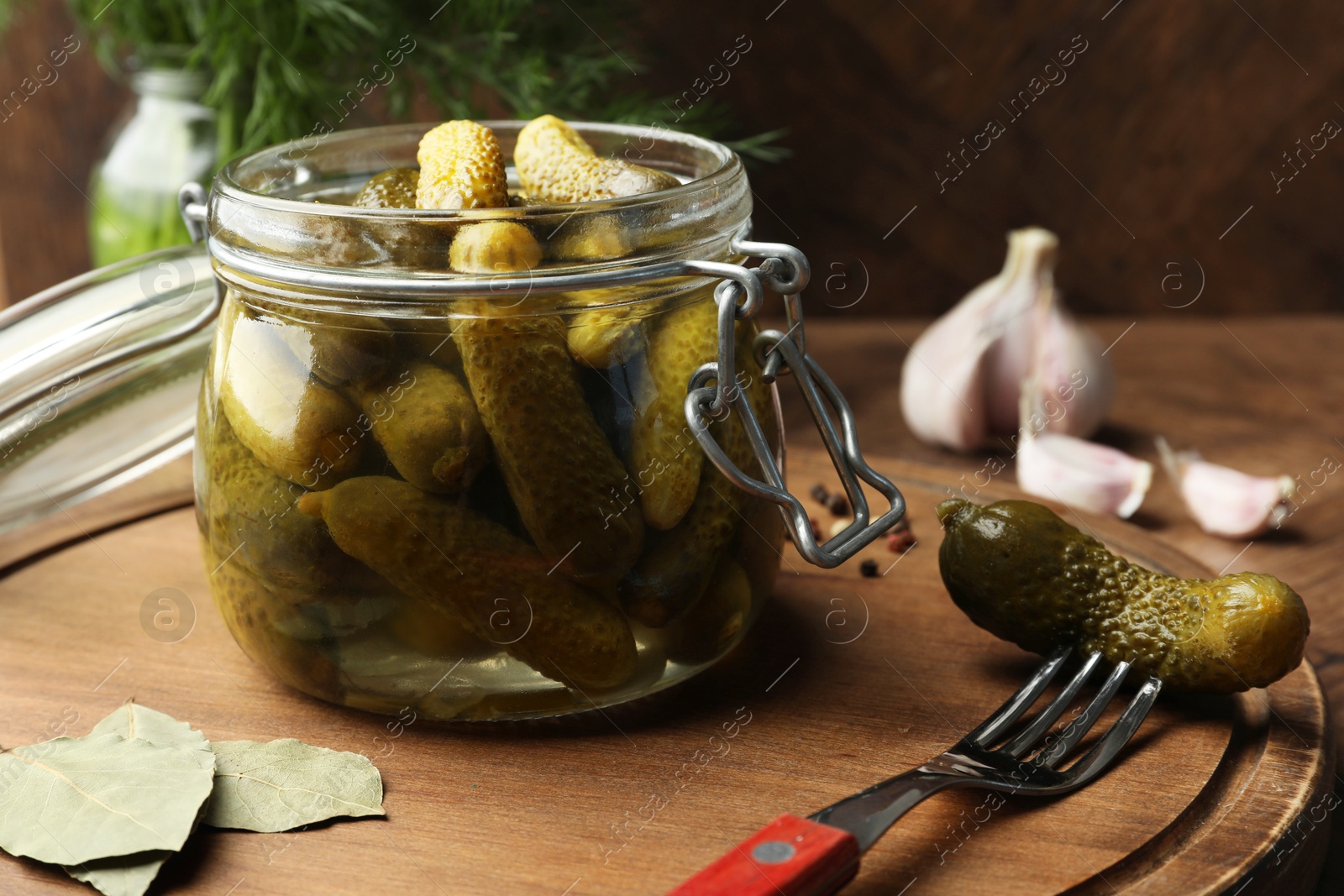 Photo of Pickled cucumbers in open jar, bay leaves and fork on table, closeup