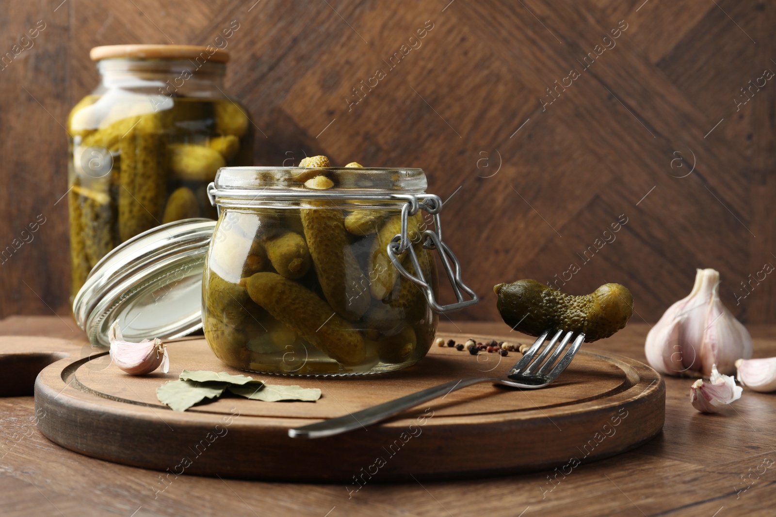 Photo of Pickled cucumbers in open jar, fork and spices on wooden table