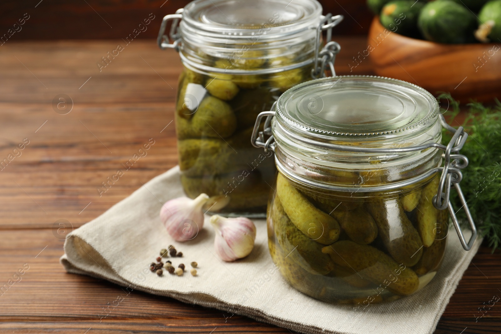 Photo of Pickled cucumbers in jars, garlic and dill on wooden table, closeup