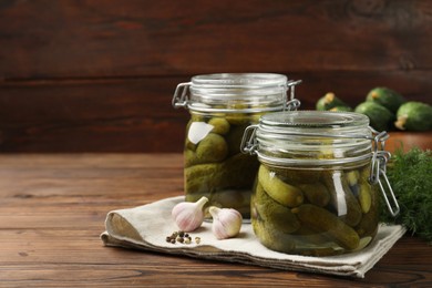 Photo of Pickled cucumbers in jars, garlic, peppercorns and dill on wooden table. Space for text