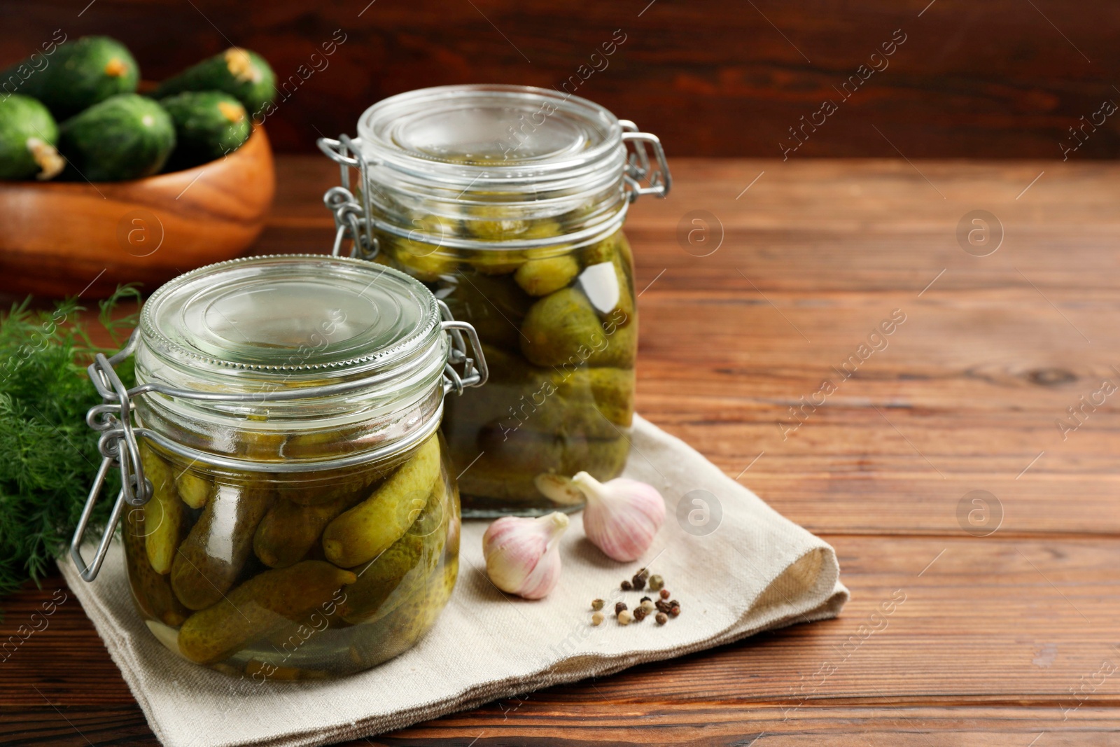 Photo of Pickled cucumbers in jars, garlic, peppercorns and dill on wooden table. Space for text