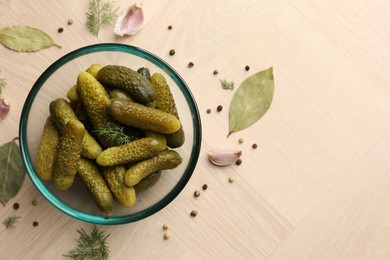 Pickled cucumbers in bowl surrounded by spices on light wooden table, flat lay. Space for text