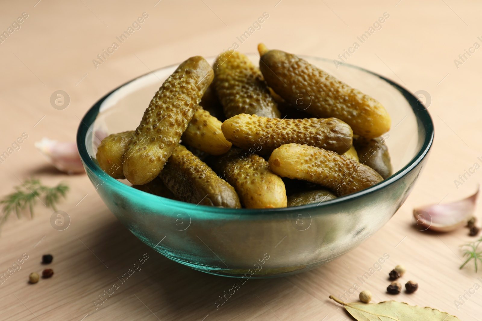 Photo of Pickled cucumbers in bowl and spices on light wooden table, closeup