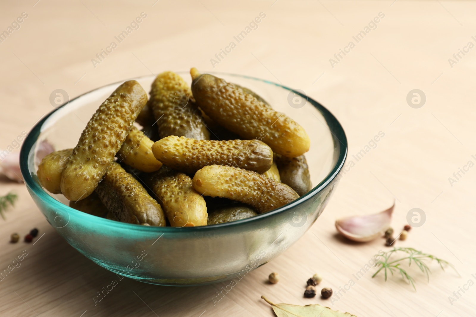 Photo of Pickled cucumbers in bowl and spices on light wooden table, closeup