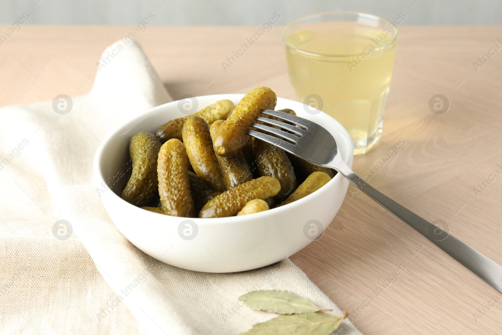 Photo of Pickled cucumbers in bowl, fork and brine on wooden table, closeup