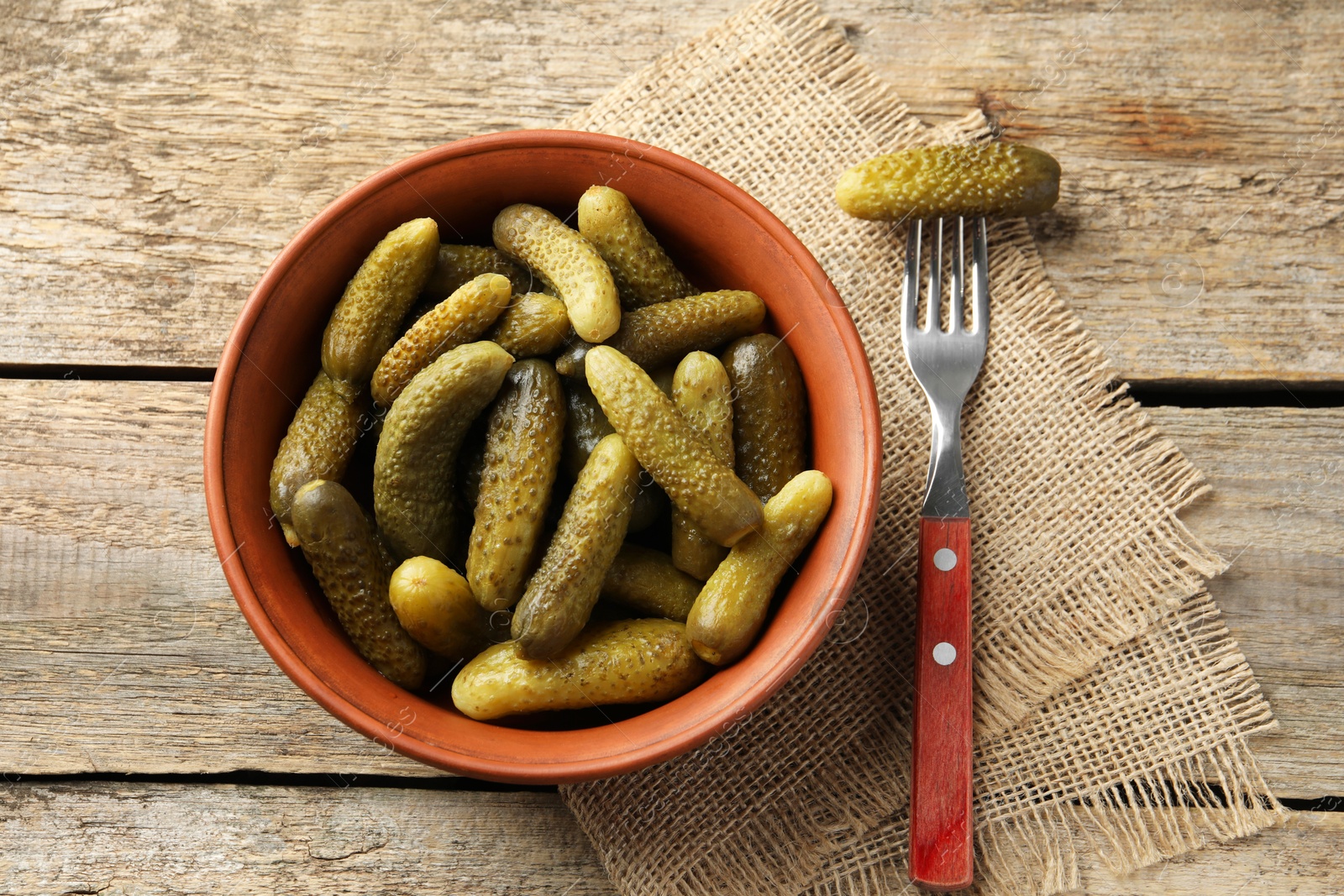 Photo of Pickled cucumbers in bowl and fork on wooden table, flat lay