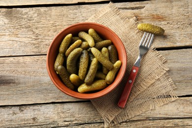 Pickled cucumbers in bowl and fork on wooden table, flat lay