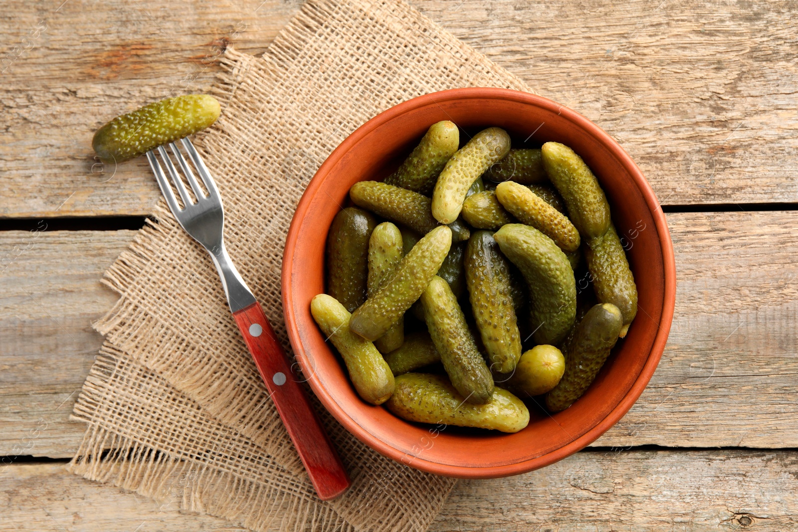 Photo of Pickled cucumbers in bowl and fork on wooden table, flat lay