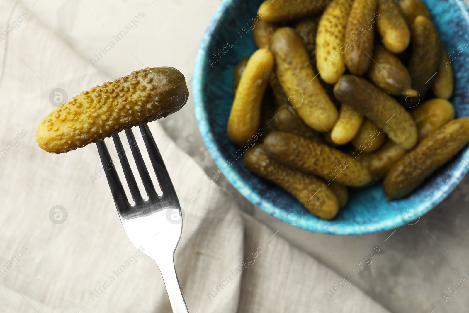 Photo of Fork with pickled cucumber and bowl full of ones on table, top view