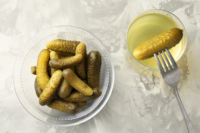 Photo of Pickled cucumbers in bowl, fork and brine on grey textured table, flat lay