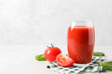 Tasty tomato juice in glass, basil leaves and fresh vegetables on light table, space for text