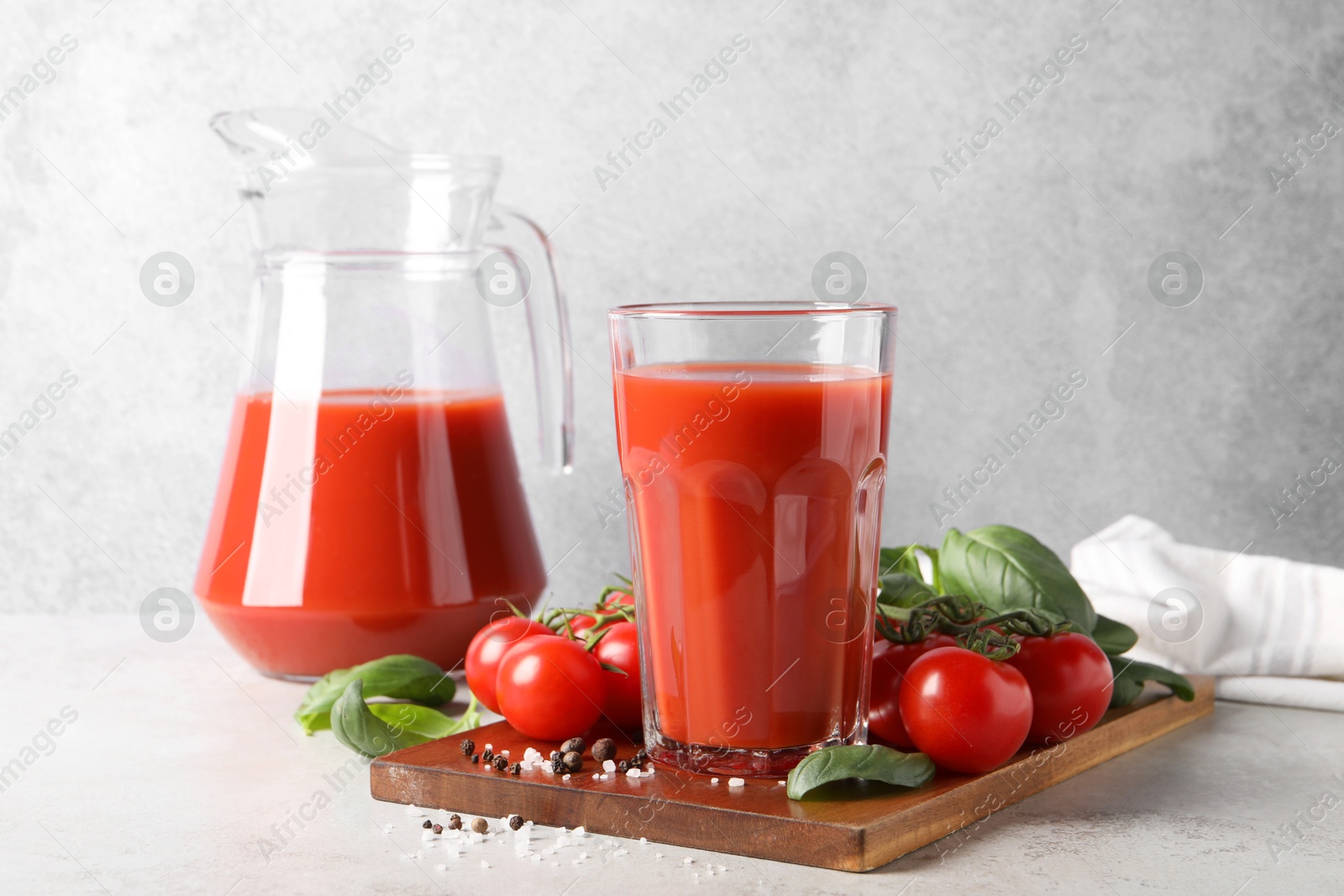 Photo of Tasty tomato juice with spices and fresh vegetables on light table