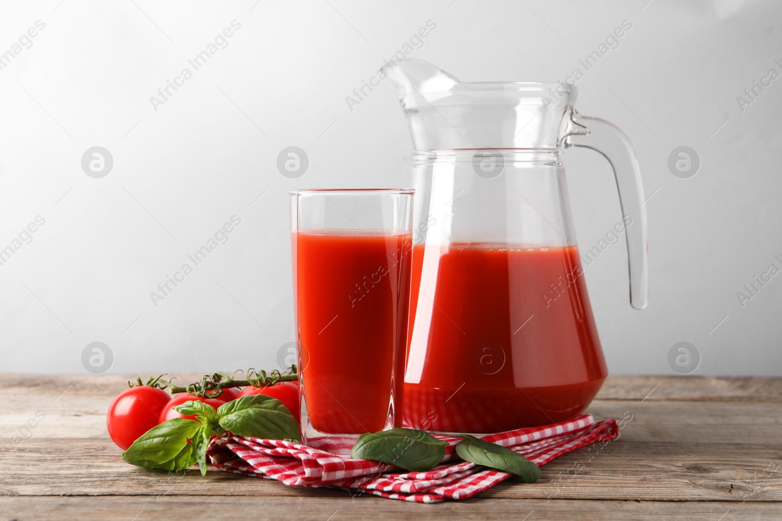 Photo of Tasty tomato juice with basil leaves and fresh vegetables on wooden table