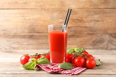 Photo of Tasty tomato juice in glass with basil leaves and fresh vegetables on wooden table