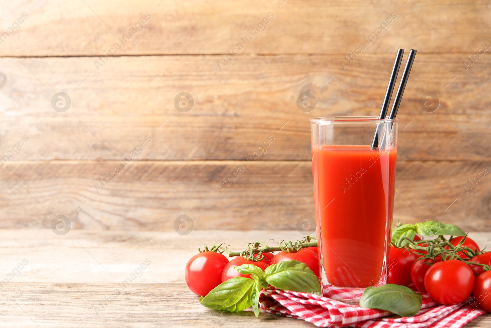 Photo of Tasty tomato juice in glass with basil leaves and fresh vegetables on wooden table, space for text