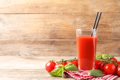 Photo of Tasty tomato juice in glass with basil leaves and fresh vegetables on wooden table, space for text