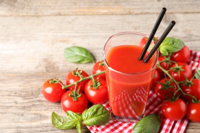 Tasty tomato juice in glass with basil leaves and fresh vegetables on wooden table, space for text