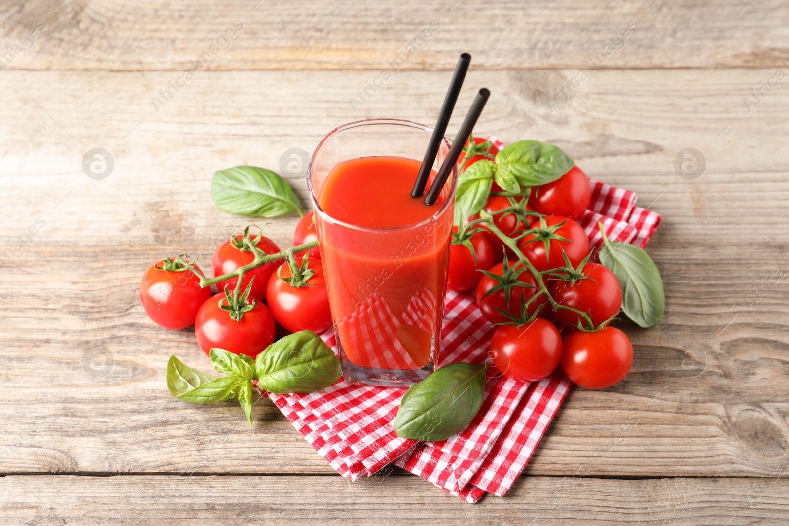 Photo of Tasty tomato juice in glass with basil leaves and fresh vegetables on wooden table