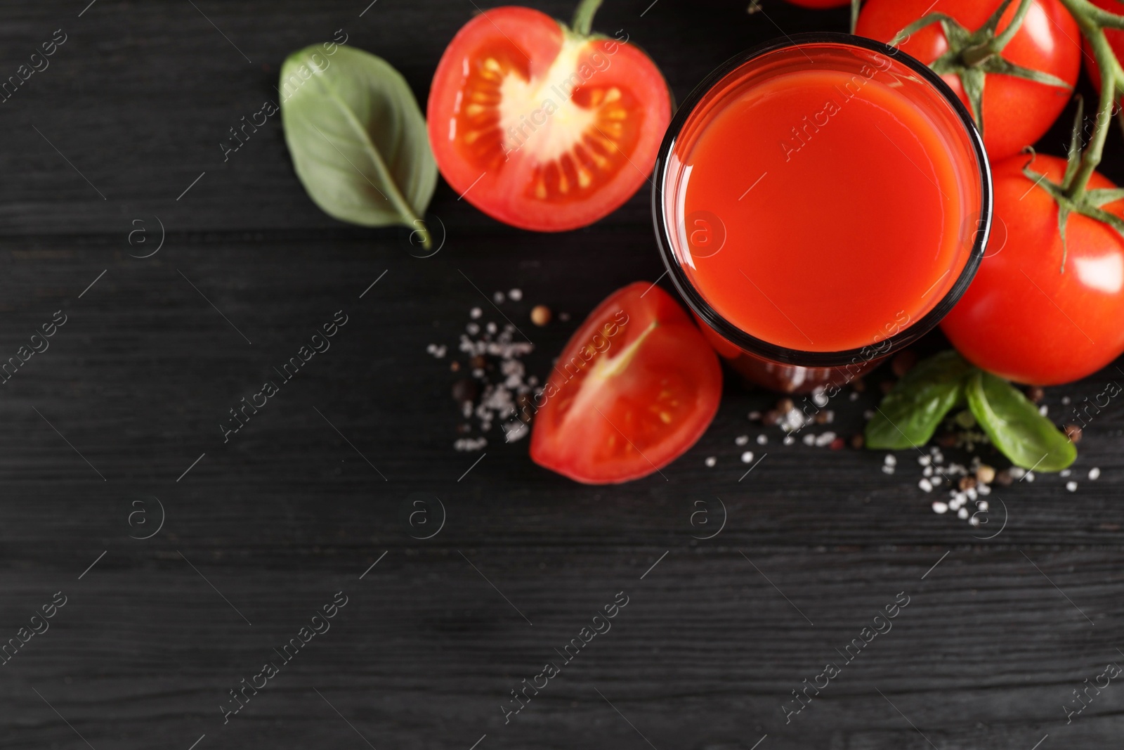 Photo of Tasty tomato juice in glass with fresh vegetables and spices on black wooden table, flat lay. Space for text