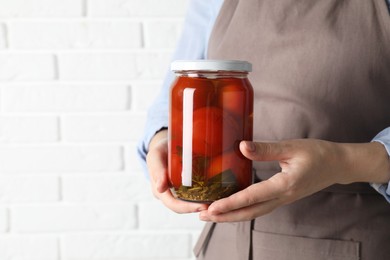 Woman holding jar with tasty pickled tomatoes against white brick wall, closeup. Space for text