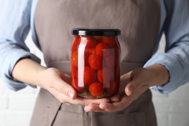 Photo of Woman holding jar with tasty pickled tomatoes on light background, closeup