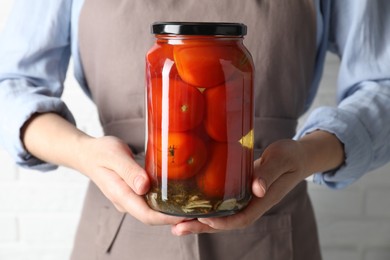 Photo of Woman holding jar with tasty pickled tomatoes on light background, closeup