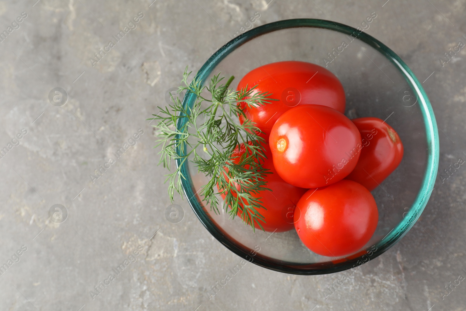 Photo of Tasty pickled tomatoes and dill in bowl on grey table, top view. Space for text