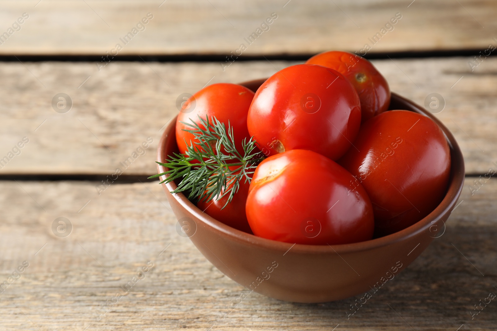 Photo of Tasty pickled tomatoes and dill in bowl on wooden table