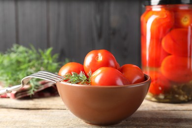 Tasty pickled tomatoes, dill and fork on wooden table