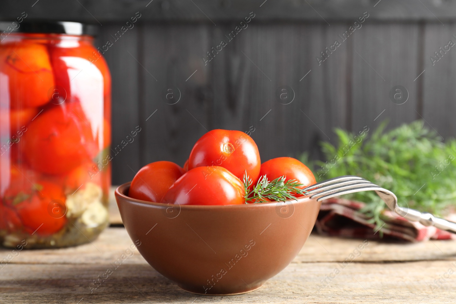 Photo of Tasty pickled tomatoes, dill and fork on wooden table