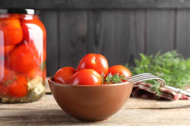 Tasty pickled tomatoes, dill and fork on wooden table