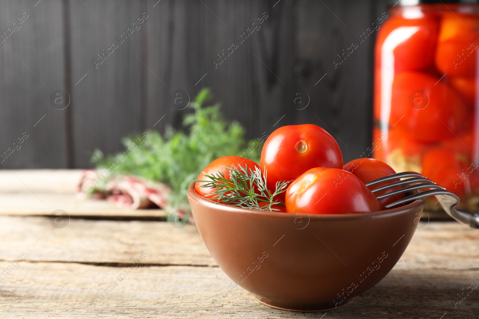 Photo of Tasty pickled tomatoes, dill and fork on wooden table, space for text