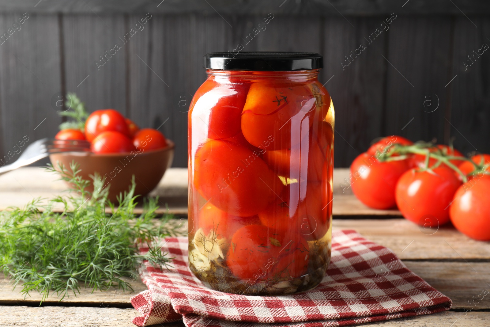 Photo of Tasty pickled tomatoes in jar, dill and fresh vegetables on wooden table