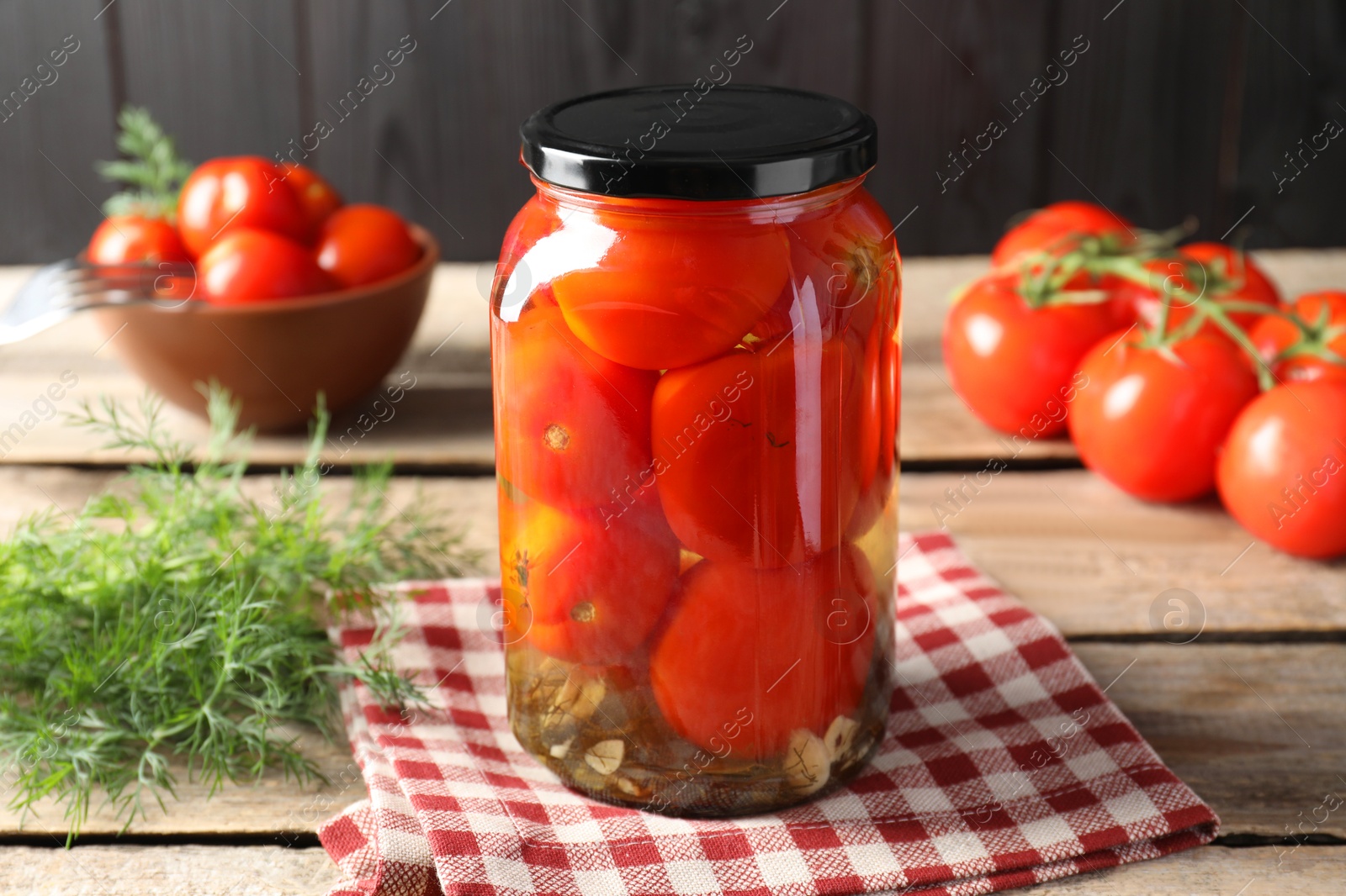 Photo of Tasty pickled tomatoes in jar, dill and fresh vegetables on wooden table